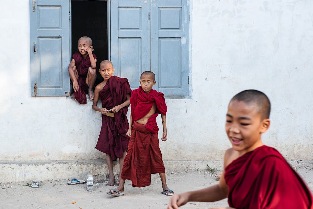 Cheerful young Buddhist novice monks playing outside a temple, wearing traditional robes.
